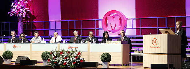 Autoridades sentadas à mesa enquanto a paraninfa discursa ao púlpito