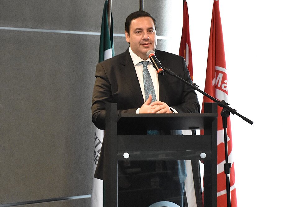 O pró-reitor está falando atrás de um pulpito, que tem o logo do Mackenzie. 