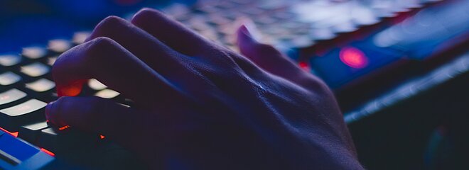 A foto mostra uma mão digitando em um teclado. A luz da foto está bem baixa. 